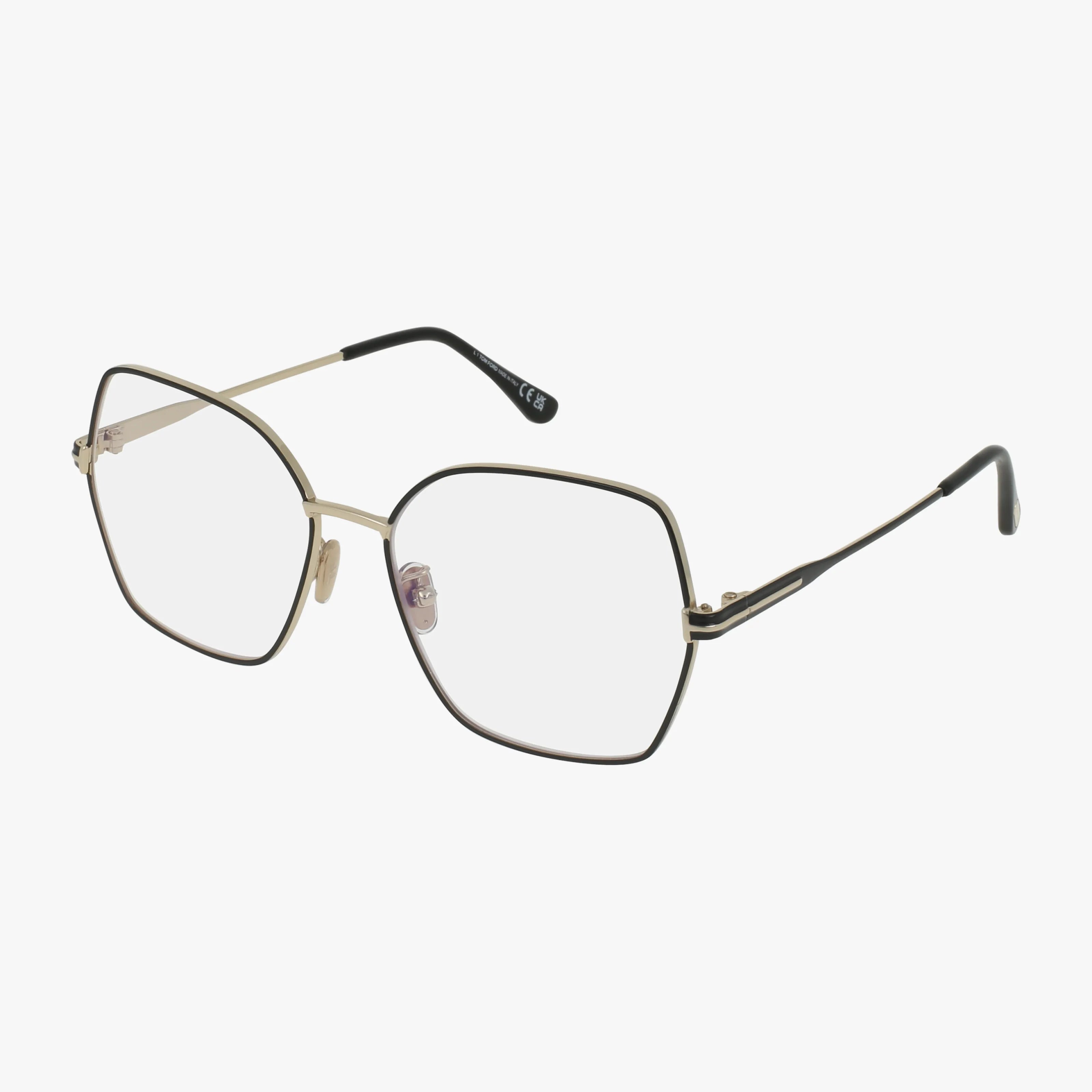 The Tom Ford FT5876-B glasses feature large, geometric thin metal frames in gold with black accents and black-tipped temples. Inspired by the 70s, these oversized clear-lensed glasses are shown angled on a white background.